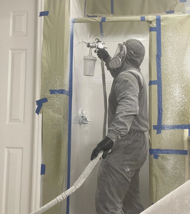 Castillo Epoxy technician in full protective gear spraying a shower enclosure.